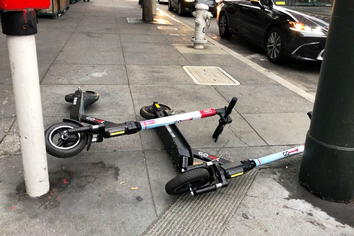 Two e-scooters lying on the sidewalk.