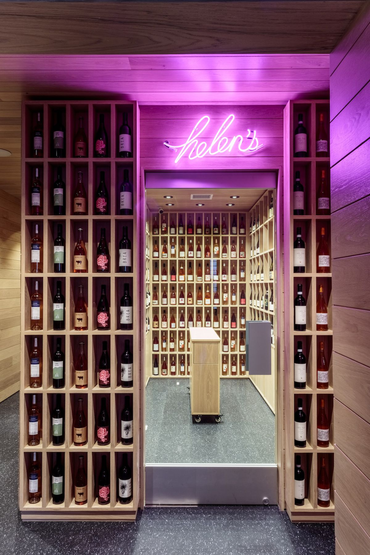 A vertical restaurant wine bar area with bottles shown in open wood nooks.
