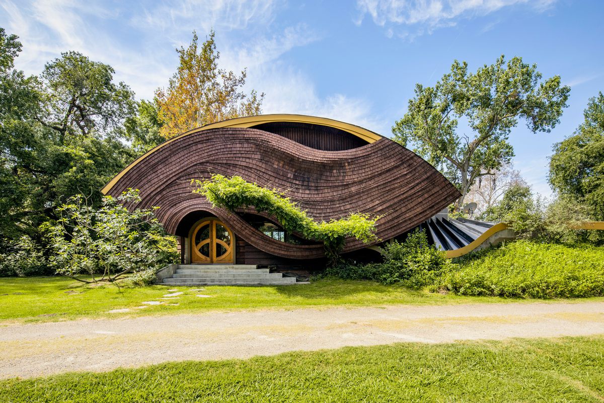 A football-shaped house with undulating wood shingles on the facade.