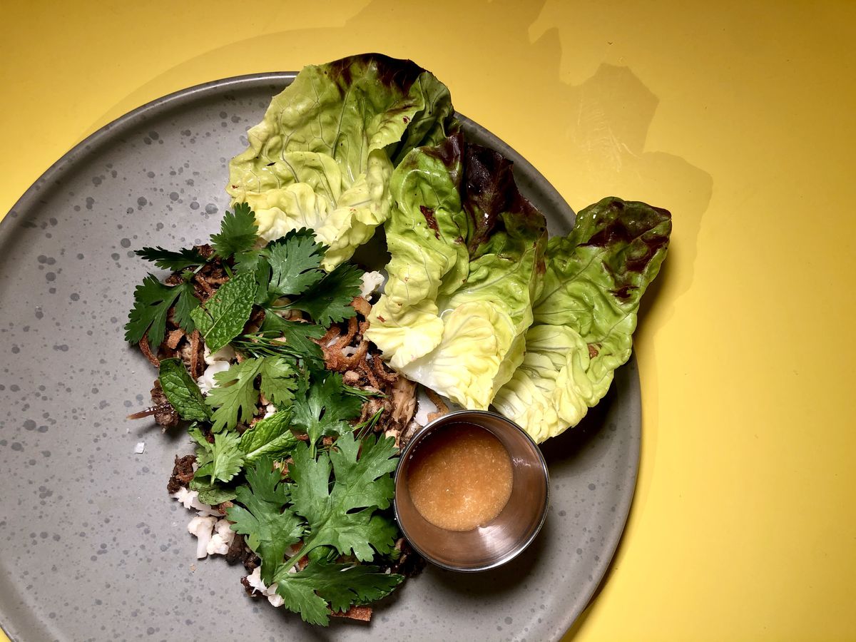A grey plate of mushroom larb at Collab Kitchen comes with pieces of little gem lettuce and a small container of sauce.