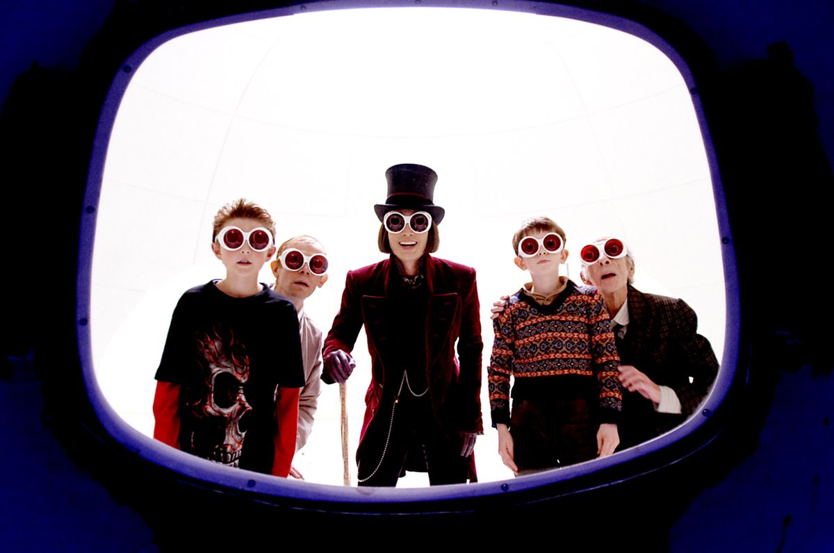 A collection of characters from Tim Burton’s Charlie and the Chocolate Factory, all wearing protective goggles, flank Willy Wonka (Johnny Depp) as they peer through an opening the shape of a television screen