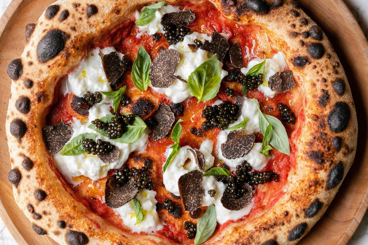 A close overhead shot of a blistered pizza with caviar and truffle and basil.