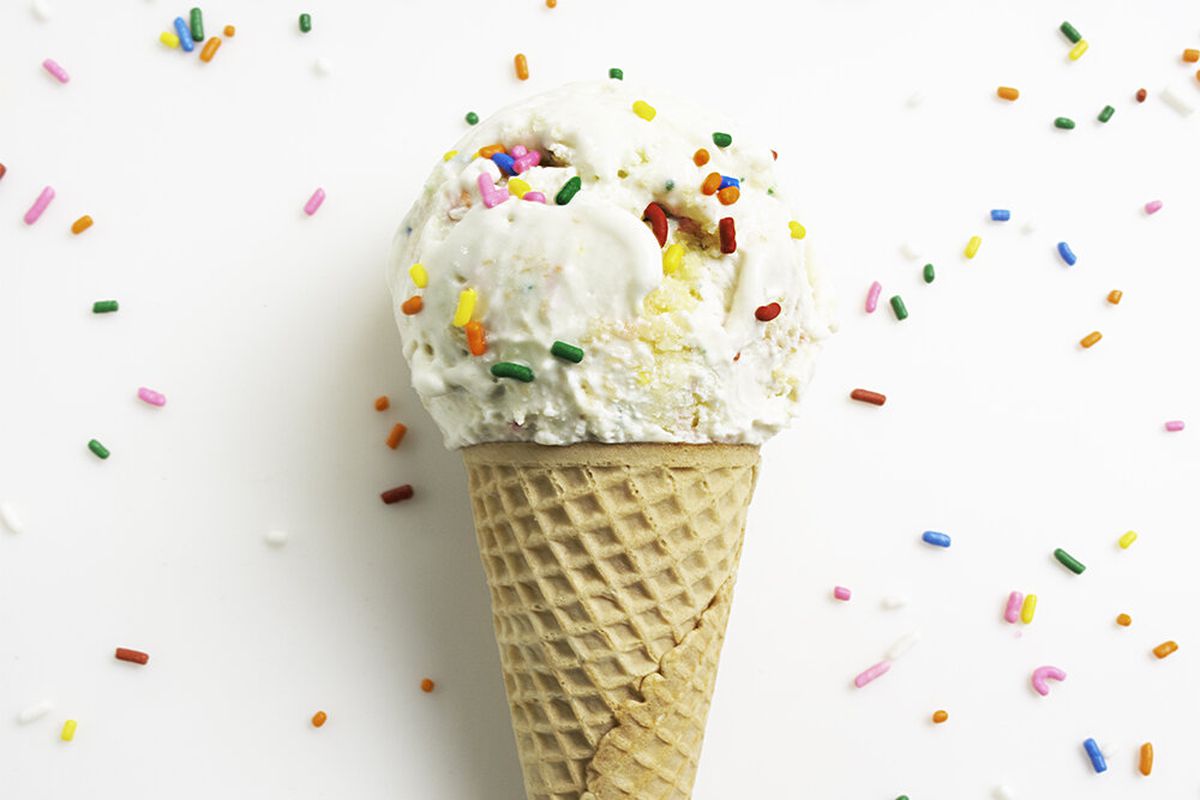 A scoop of ice cream in a cone with sprinkles on a white background with sprinkles.