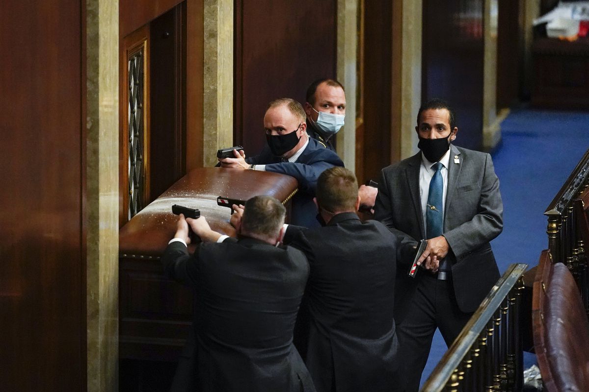 Capitol Police with guns drawn stand near a barricaded door as rioters try to break into the House Chamber.