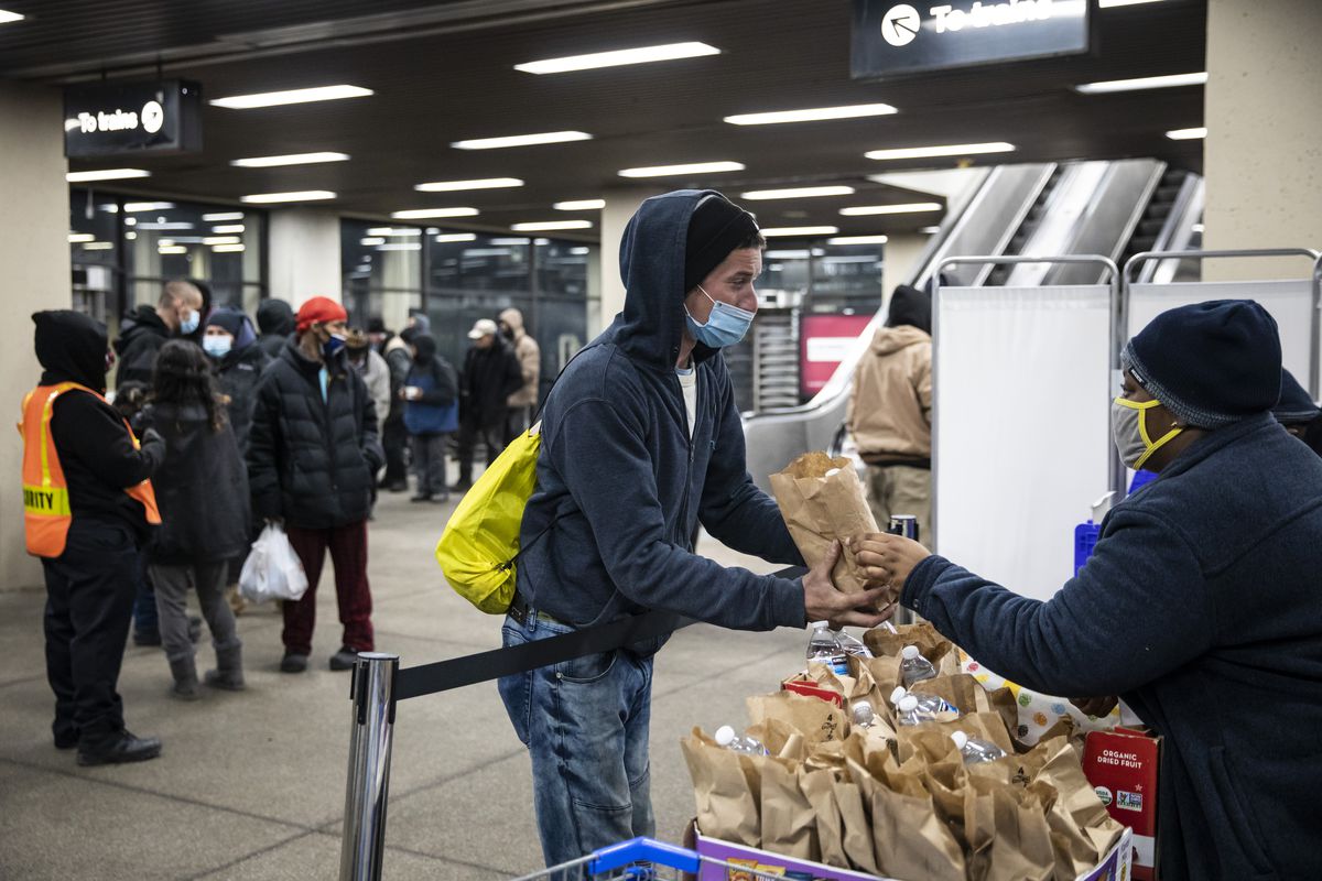 Kyanna Johnson, a public ally at the Night Ministry, hands a bag of food to a homeless person as the non-profit offers free health care and outreach services at the CTA’s Blue Line Forest Park station, Wednesday night, Feb. 23, 2021. | Ashlee Rezin Garcia/Sun-Times