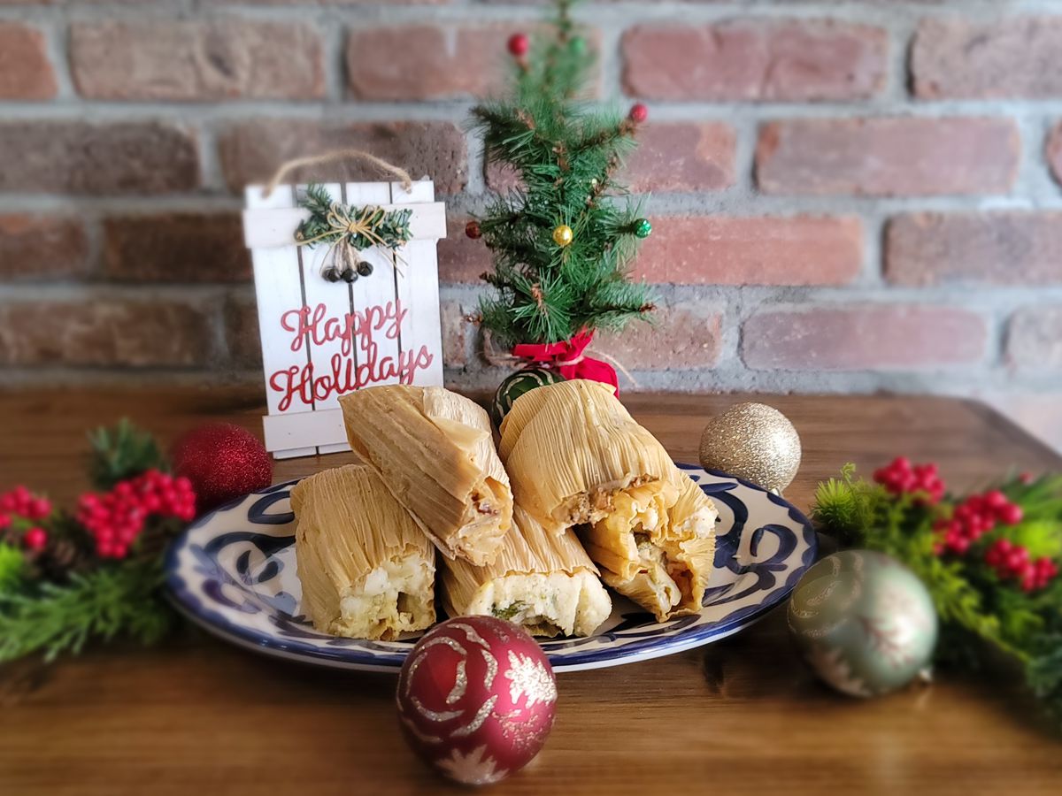 A plate of tamales surrounded by holly and ornaments with a sign reading Happy Holidays in the background.