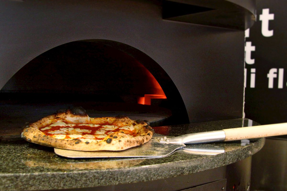 A pizza being pulled out of a pizza oven
