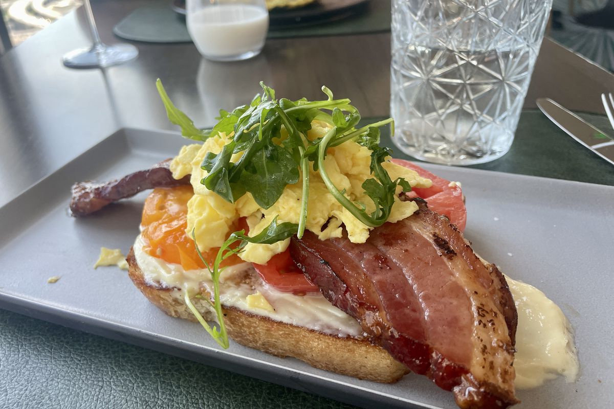 A plate holds a piece of toast with eggs, bacon, tomatoes, and lettuce.
