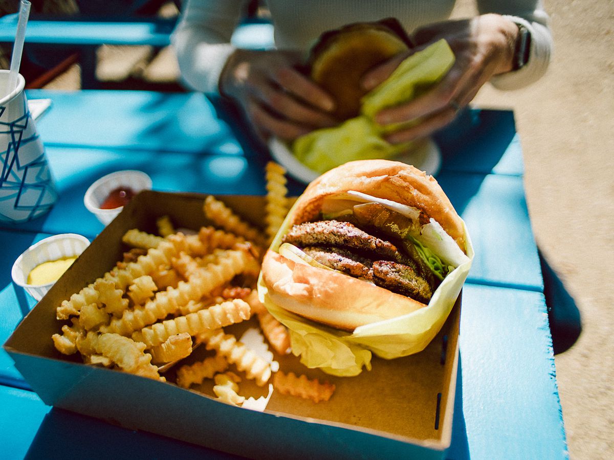 A burger in a paper wrap and fries in a tray on a blue picnic table.