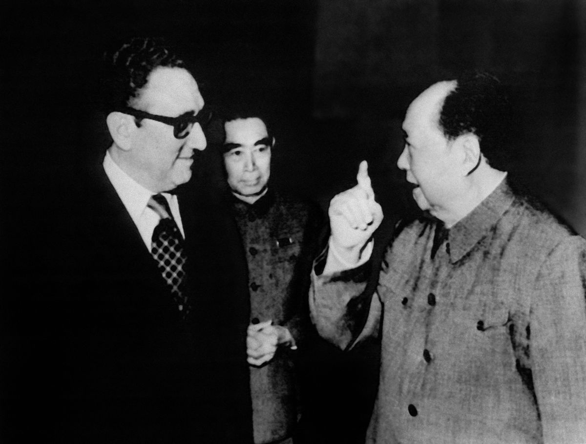 Kissinger, Zhou, and Mao in a black-and-white image, as they walk and talk together.
