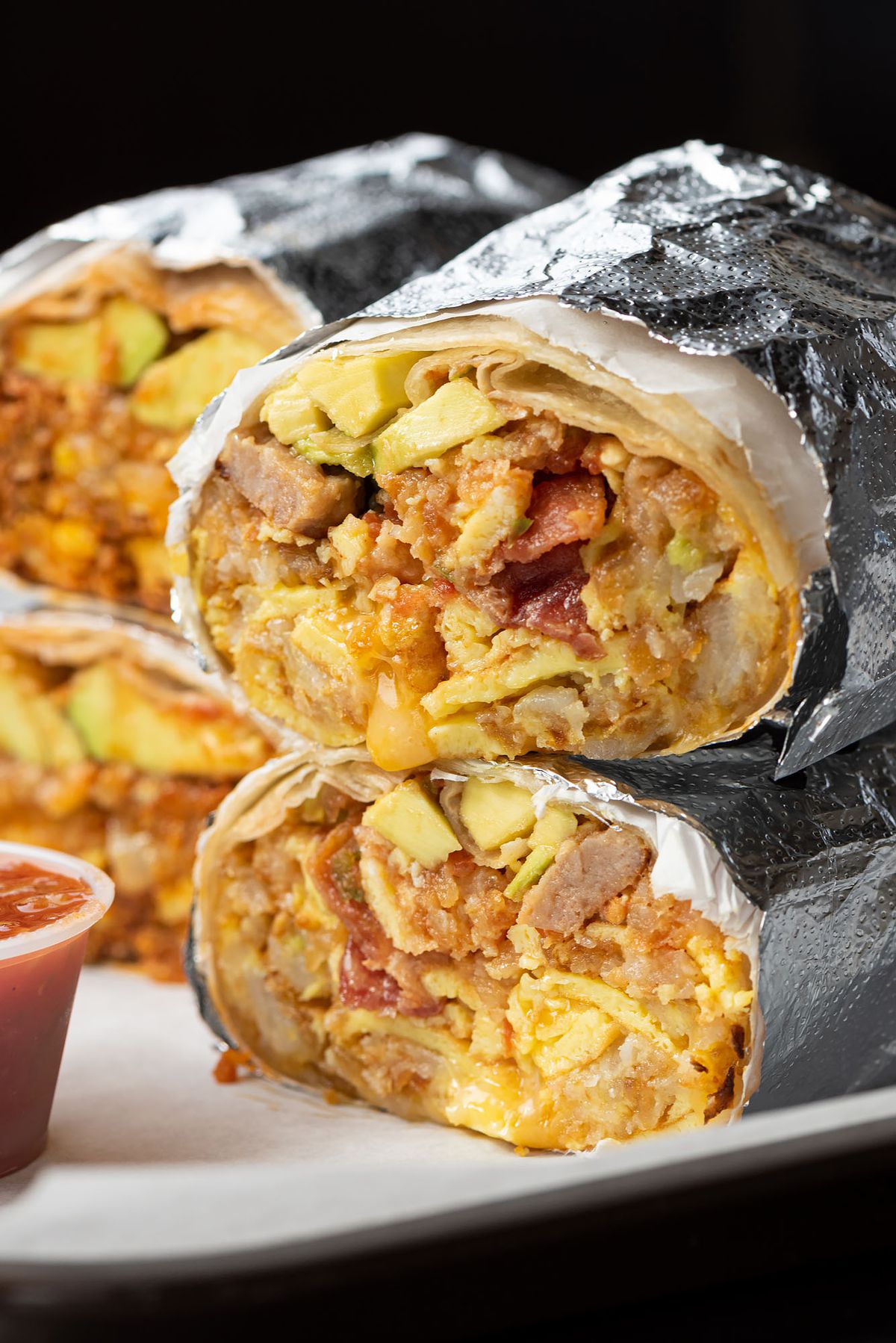 Stacks of breakfast burritos dripping with cheese.