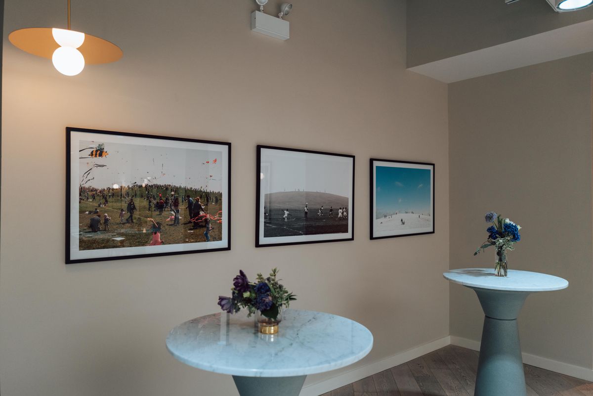 Three photos of the same hill in a row on a beige wall, with two marble-topped tables in the foreground