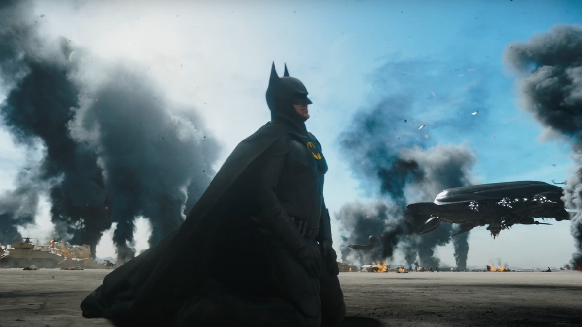 Batman kneels in the desert, surrounded by smoke plumes, with a spaceship visible in the background