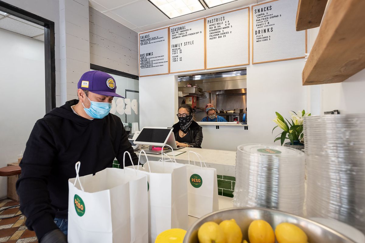 A masked worker in a purple hat handles food for delivery.