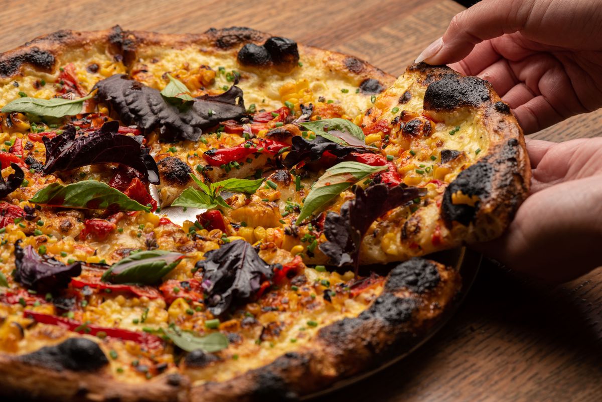 A hand reaches in from the side to pull a piece of a heavily-charred pizza.