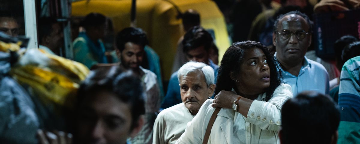 Aunjanue Ellis-Taylor walks through a crowd of Indian people, looking disoriented and hot, in Origin