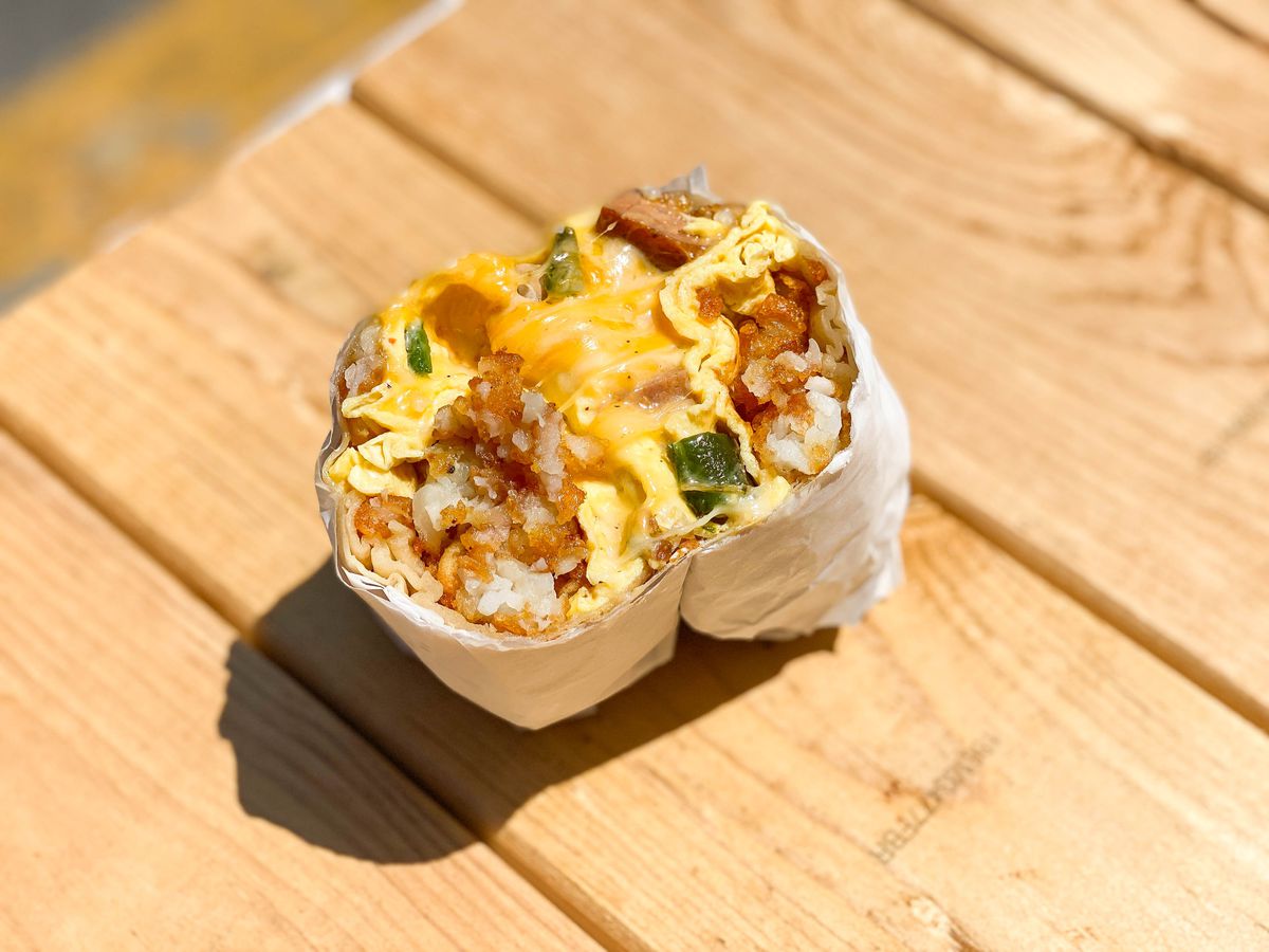 A side angle view of a split breakfast burrito on a bright wooden bench.
