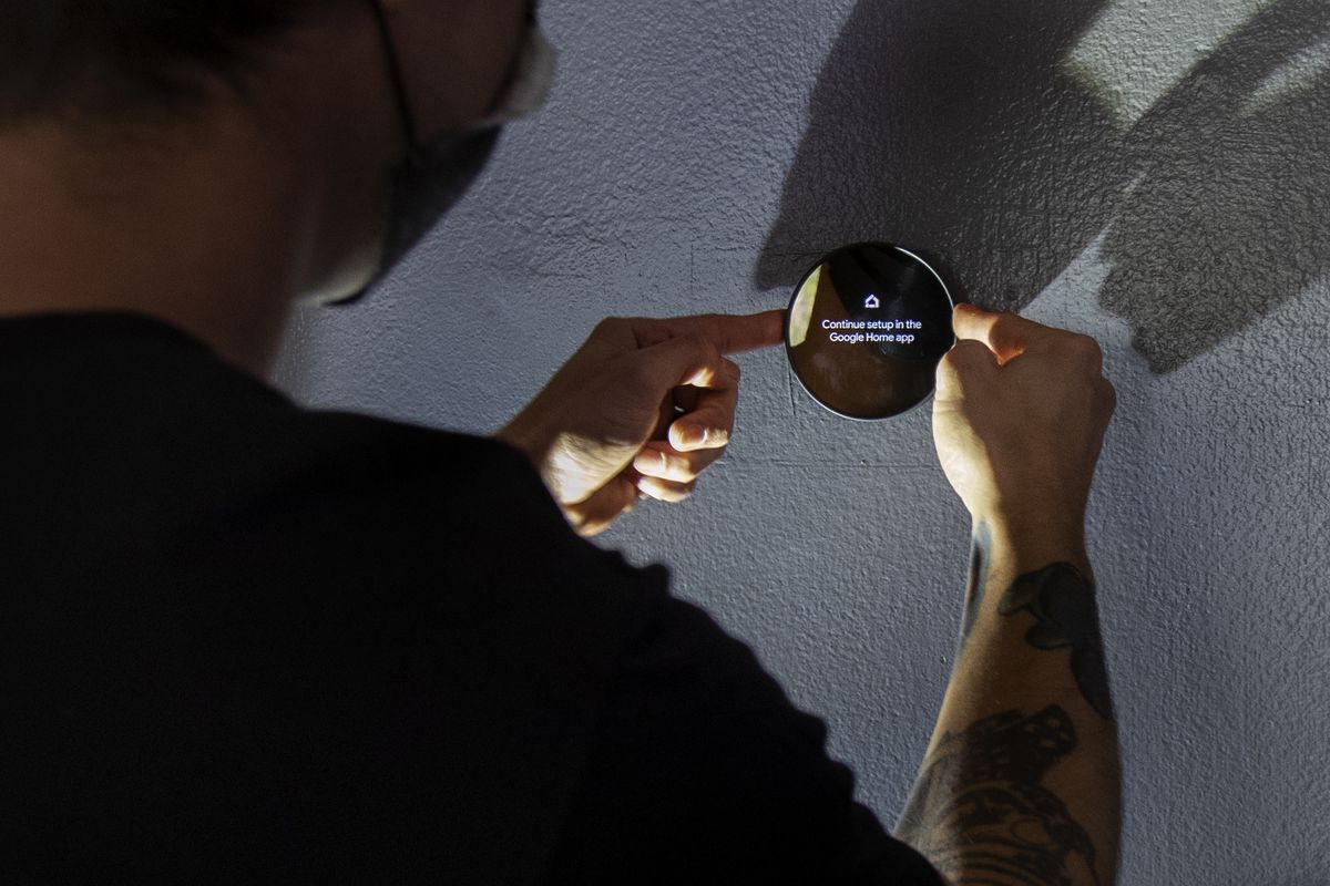 A person operating a Google Nest smart thermostat.