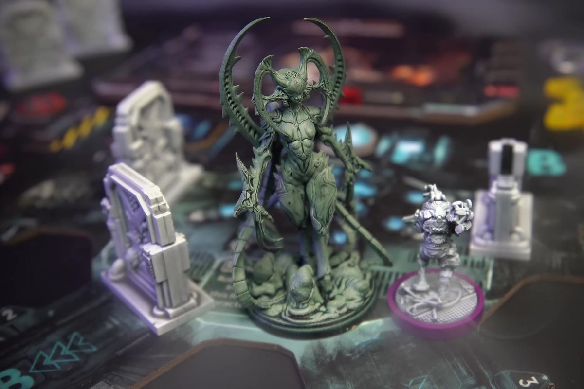 A xenomorph-like female-presenting alien monster, at least 20 feet tall to scale, fills a room with two possible exits. A space marine enters, woefully unprepared. The scene is from a board game, with smoke for effects.