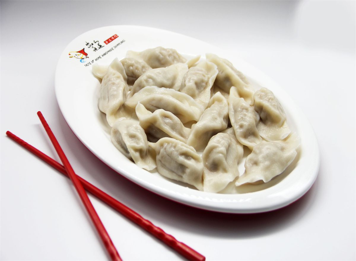A plate of steamed dumplings next to a pair of red chopsticks.