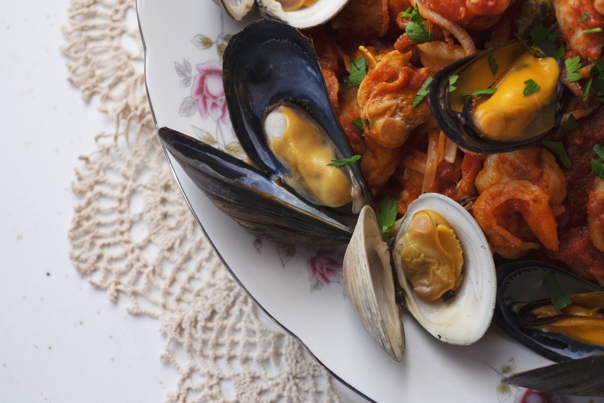 A bowl with open mussels and clams, red pasta, on a doily. 