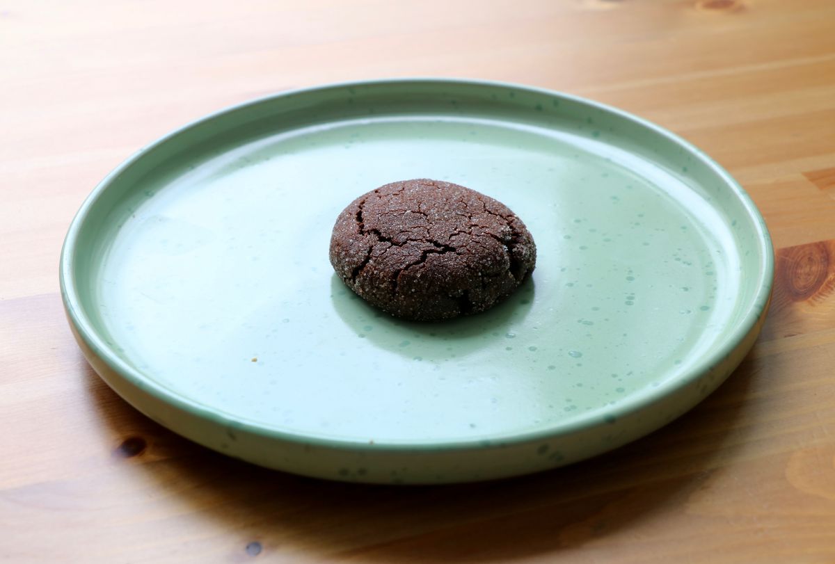 A dark chocolate cookie sits on a light wood table on a light green plate