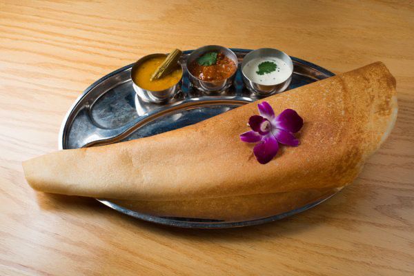 A dosa on a metal tray with sambar and various chutneys.