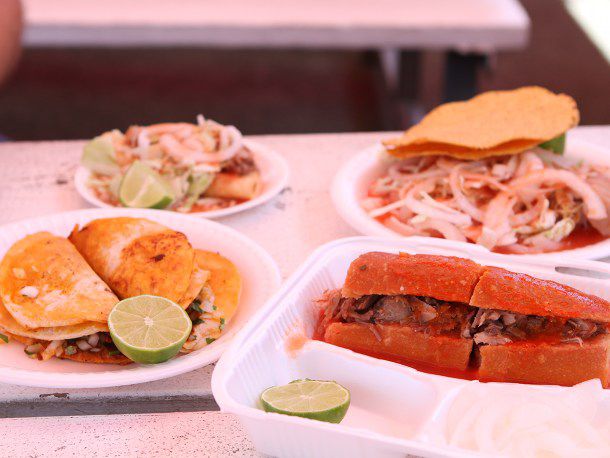A red-tinged table filled with spicy sandwiches and tacos in deeply fiery sauces.