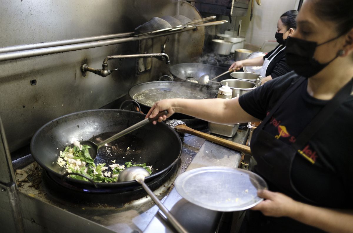 A woman wearing a black shirt cooks greens in a wok. 