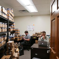 Neal Harmon, cofounder and CEO of VidAngel, right, places a phone call while Matthew Holland, left, works in the receiving room at VidAngel's office in Provo on Wednesday, July 20, 2016. Harmon's doesn't have a private office and instead works out of the spare desk in receiving.