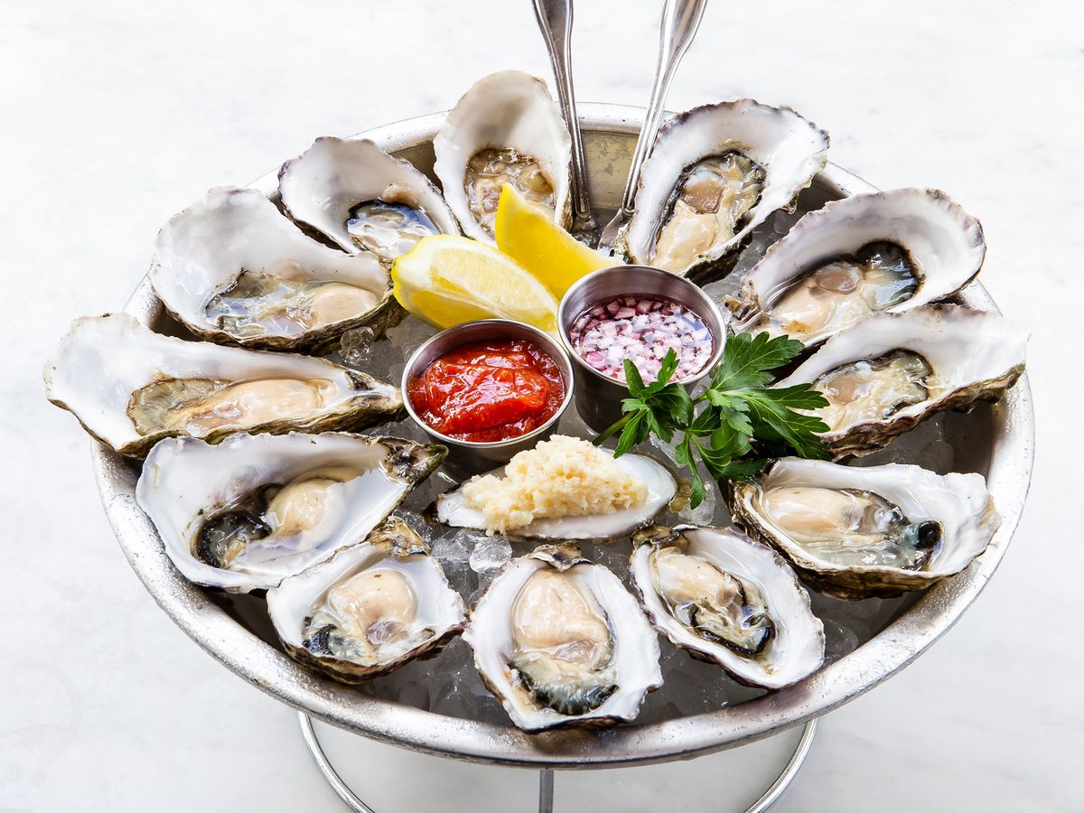 A platter of oysters with lemons and cocktail sauce in the middle. 
