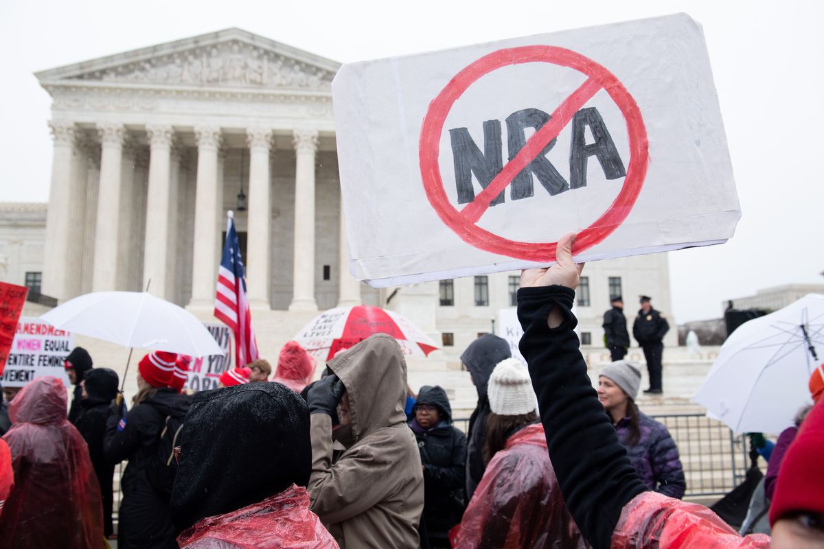 Protesters outside the Supreme Court building holds up a sign that has the red-circled letters NRA on it with a line through them.
