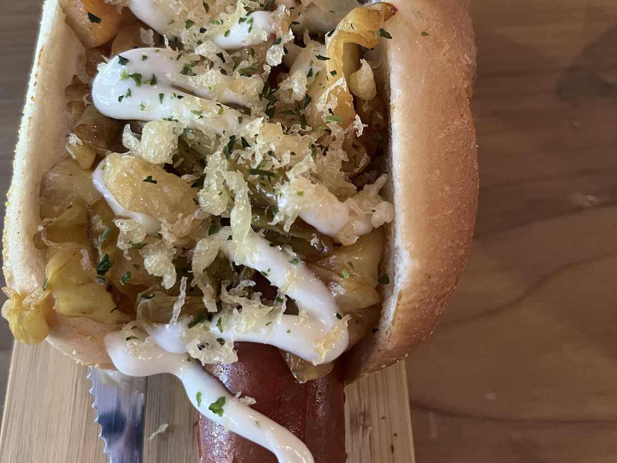 A hot dog topped with cabbage, aioli, and seaweed flakes.