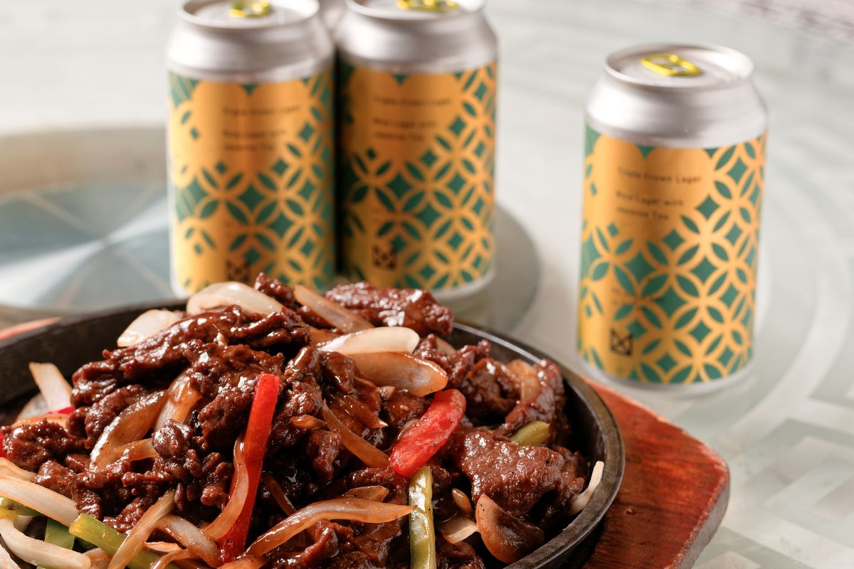 Three cans of beer in front of a sizzling platter of peppers and beef.