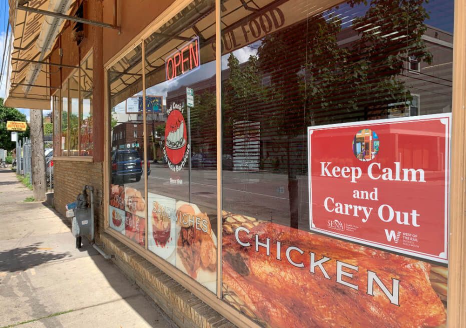 The exterior of a restaurant with large windows and a red sign that says “Keep Calm and Carry Out.’