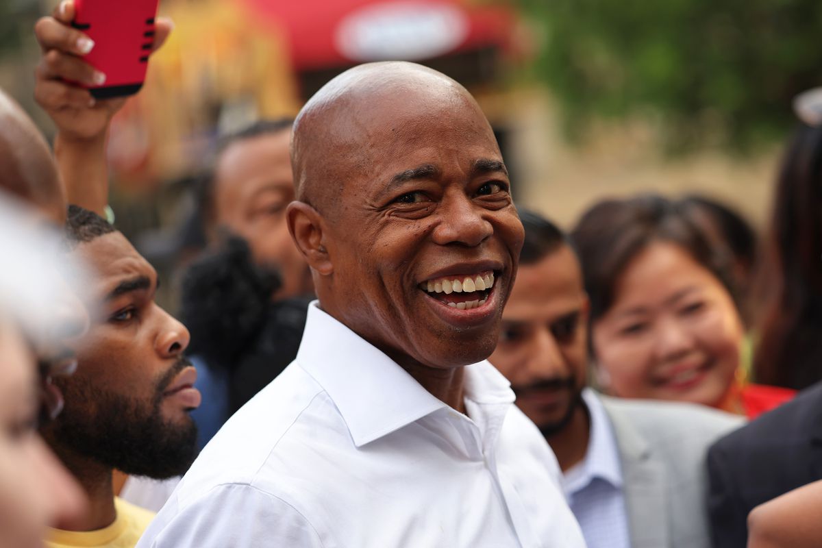 Eric Adams, wearing a white button-up shirt, smiles while surrounded by supporters ahead of the 2021 mayoral primary in New York City.