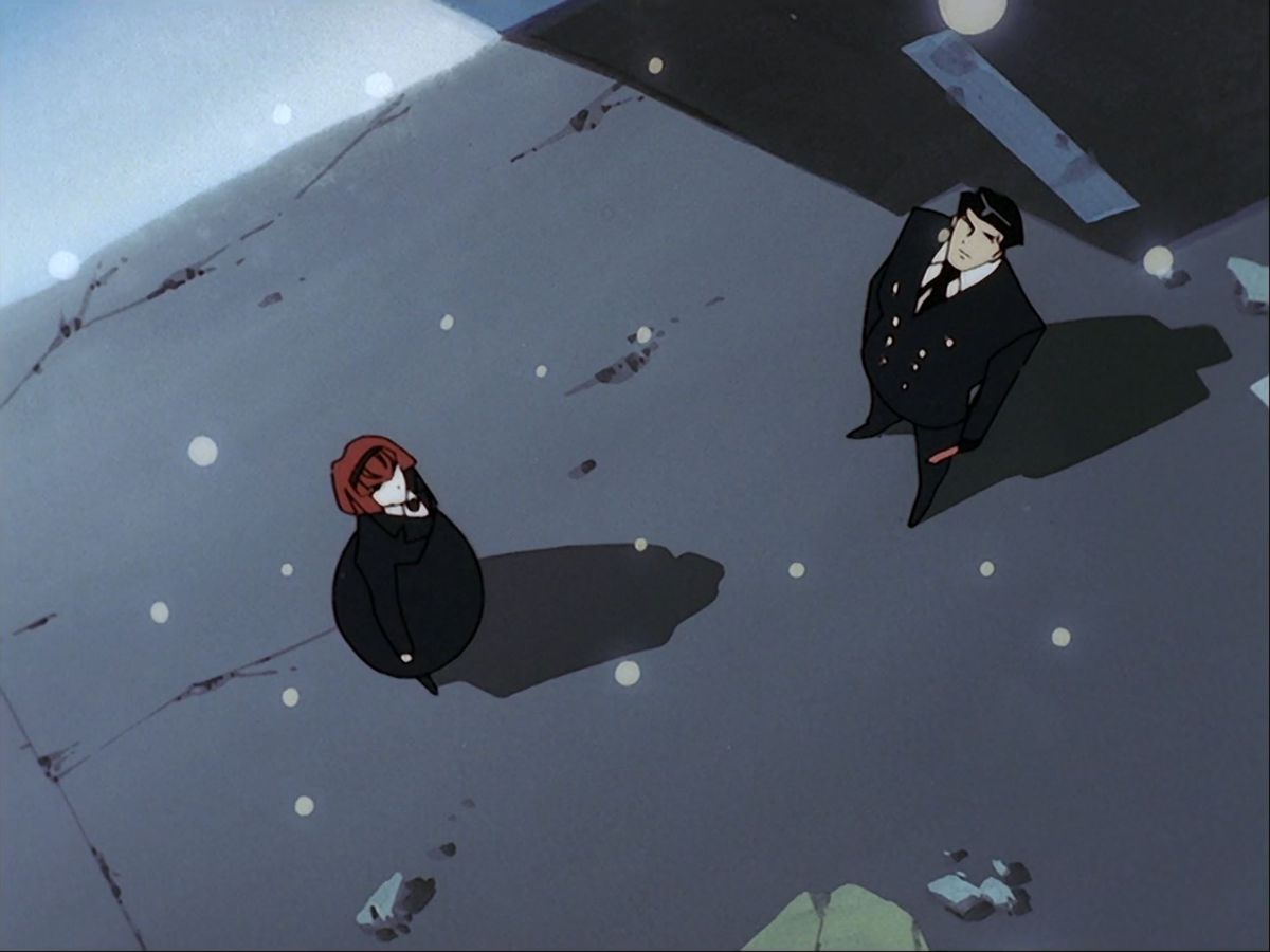 A man in a black suit and a young woman in a black dress look up as snow falls from the sky.