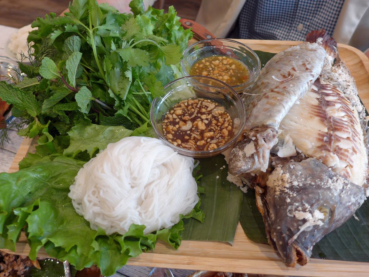 A whole fish, white rice noodles, and thicket of herbs and lettuce.