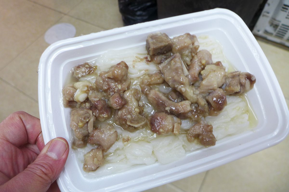 A plastic tray with white noodles underneath tiny pork ribs.