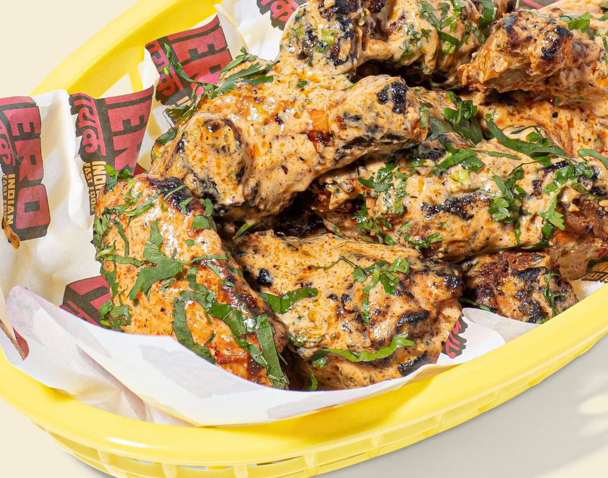 A yellow basket of butter chicken wings, with coriander on top.