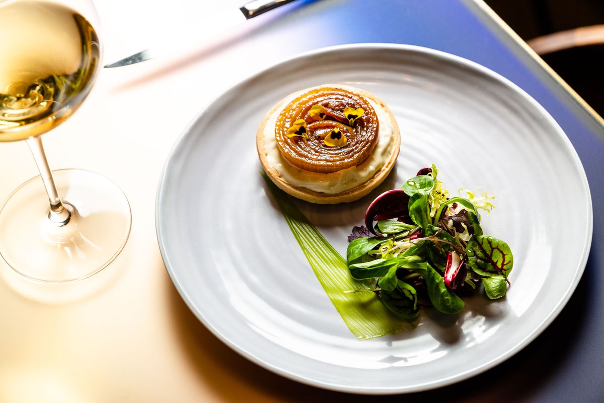 An onion tart sits on a plate next to a small green salad.
