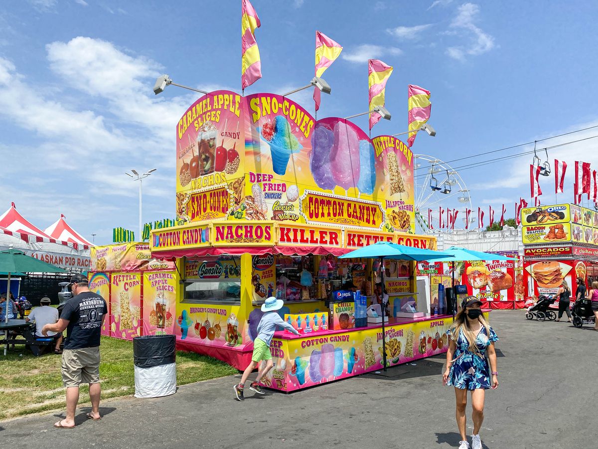 A yellow and pink food stand at a county fair with clouds behind.