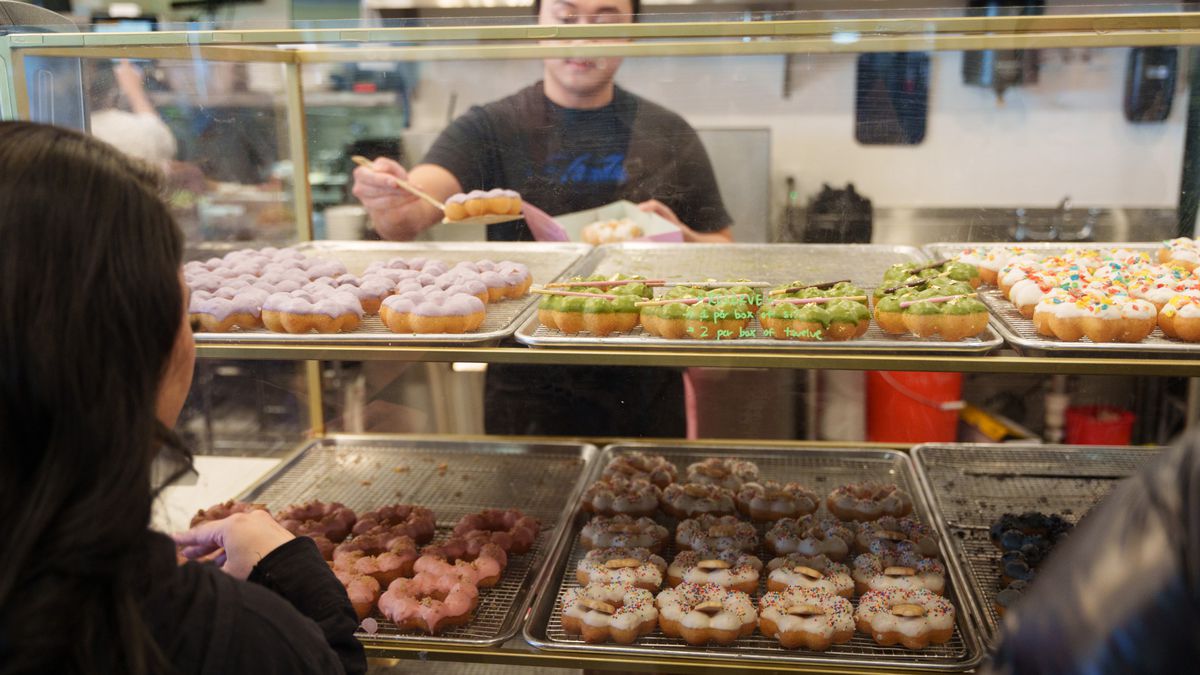 A person grabs a mochi doughnut off a bakery shelf to put it in a box. 