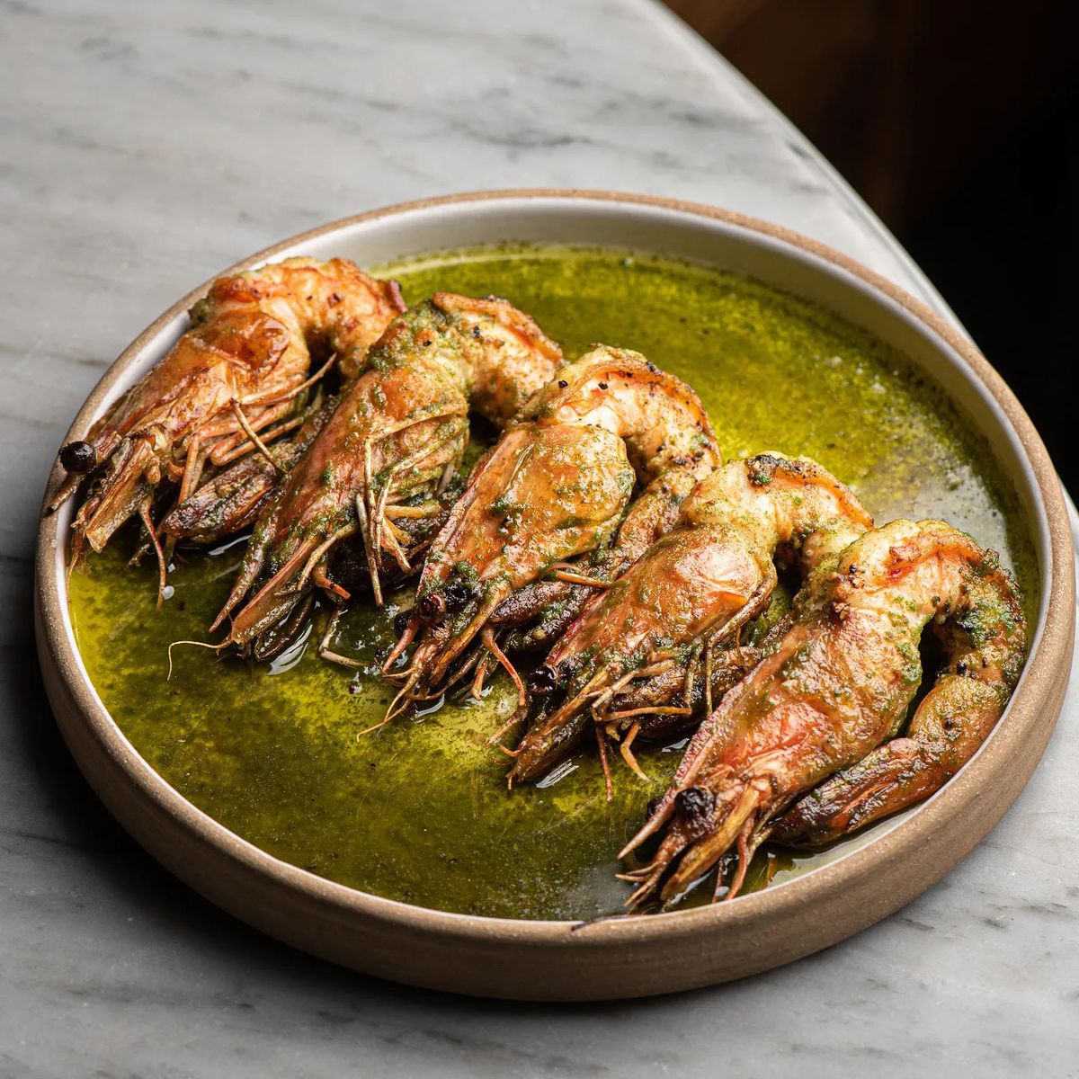 A terracotta-colored stone bowl filled with five grilled prawns and a green sauce made from herbs at Felix Trattoria.