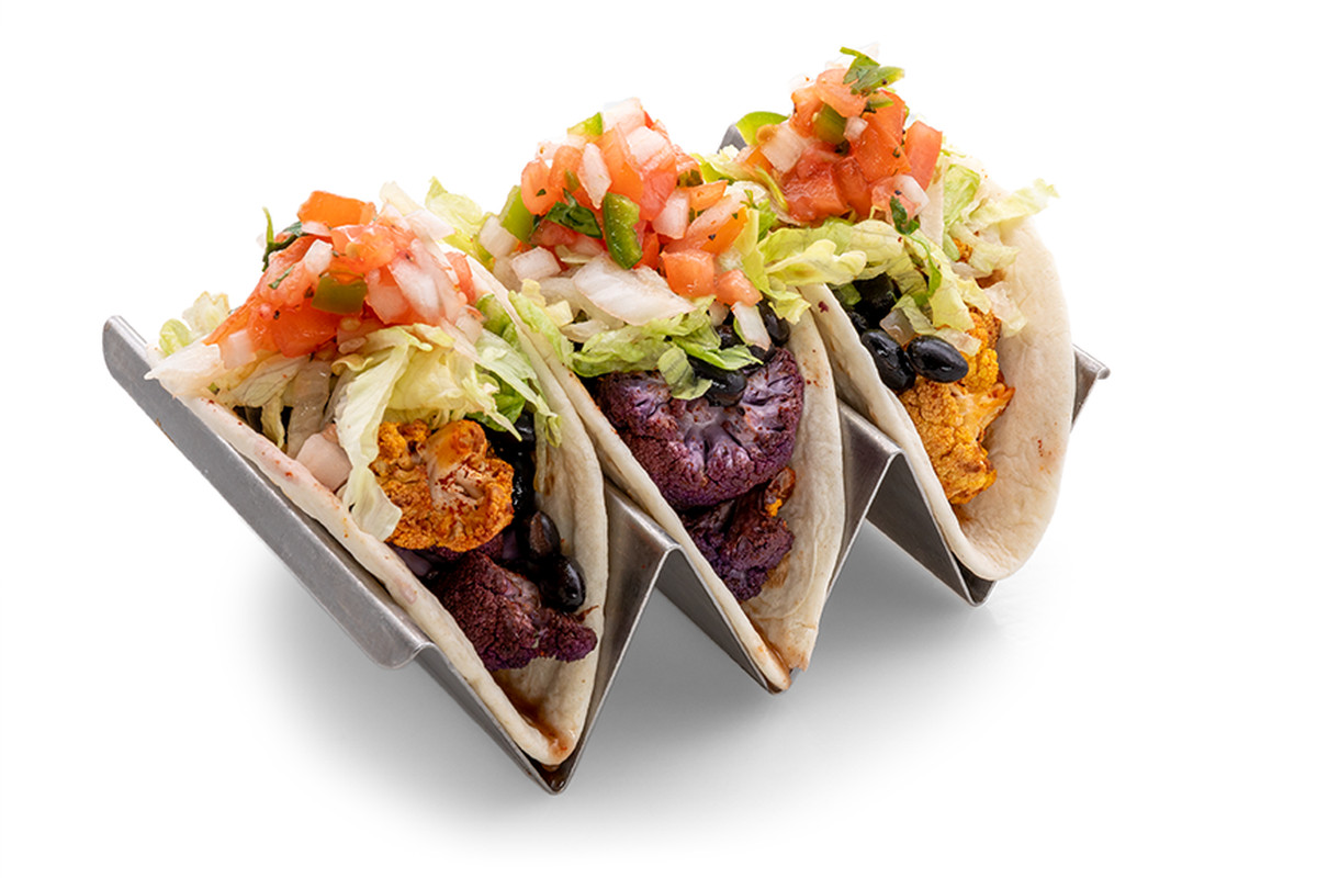 A photo of a metal holder containing three of Empower Field’s new vegetarian street tacos. A layer of Chipotle roasted cauliflower and ranchero black beans are visible inside the flour tortillas. They are topped with lettuce and salsa. 