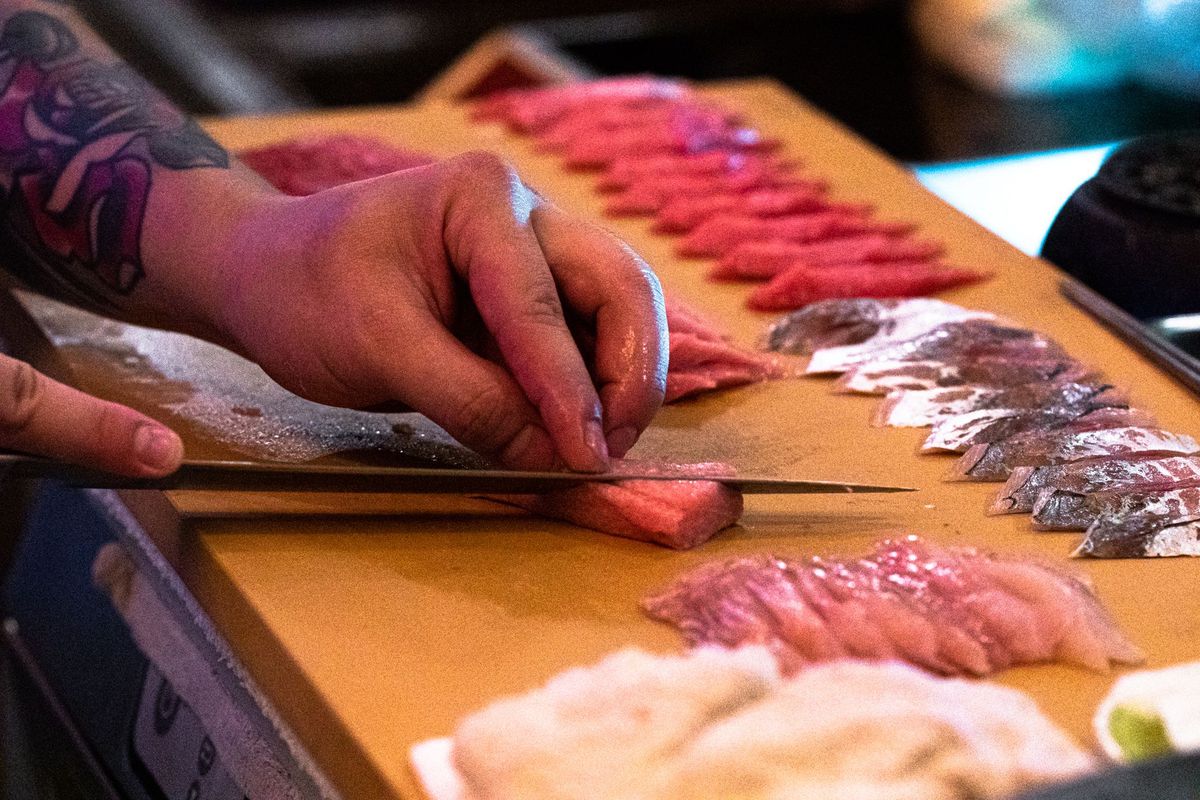 Focus on hands slicing sushi with several slices already laid out on a wooden board