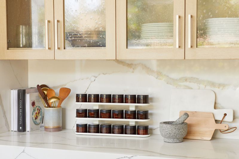 A modern spice rack in amber bottles sits on a modern kitchen counter. 