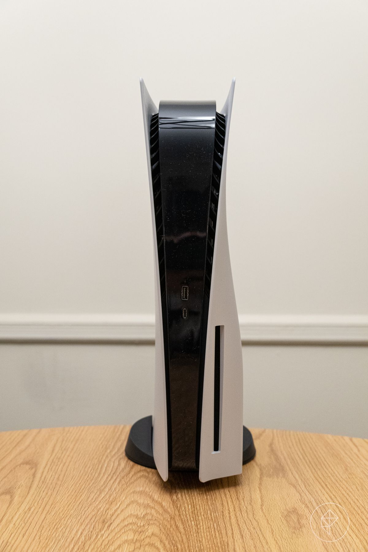 a tall photo of the PlayStation 5 standing vertically on a round wooden table