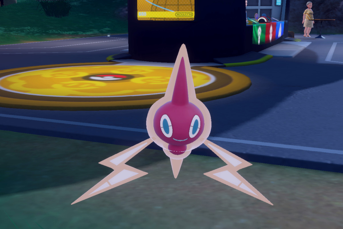 A shiny Rotom floats in front of a Pokémon Center