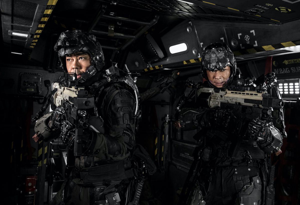 Two men in black exosuits carrying rifles in a sci-fi industrial corridoor.
